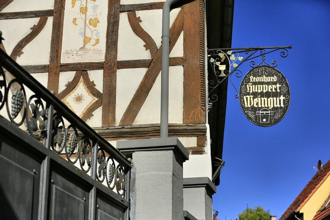 Traditionelles Wirtshausschild mit Weinrebe und Weinglas. Darauf steht in goldenen Buchstaben Leonhard Huppert Weingut.